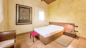 A bedroom with a bed, a bench, a rug, a nightstand with a lamp, and a framed picture on the wall. - Oliver Conti (House, Capmany) (Capmany)