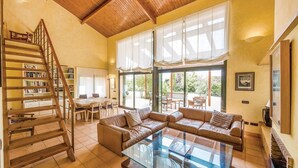 A spacious living room with a glass coffee table, leather sofas, a wooden staircase, and a large window with curtains. - Oliver Conti (House, Capmany) (Capmany)
