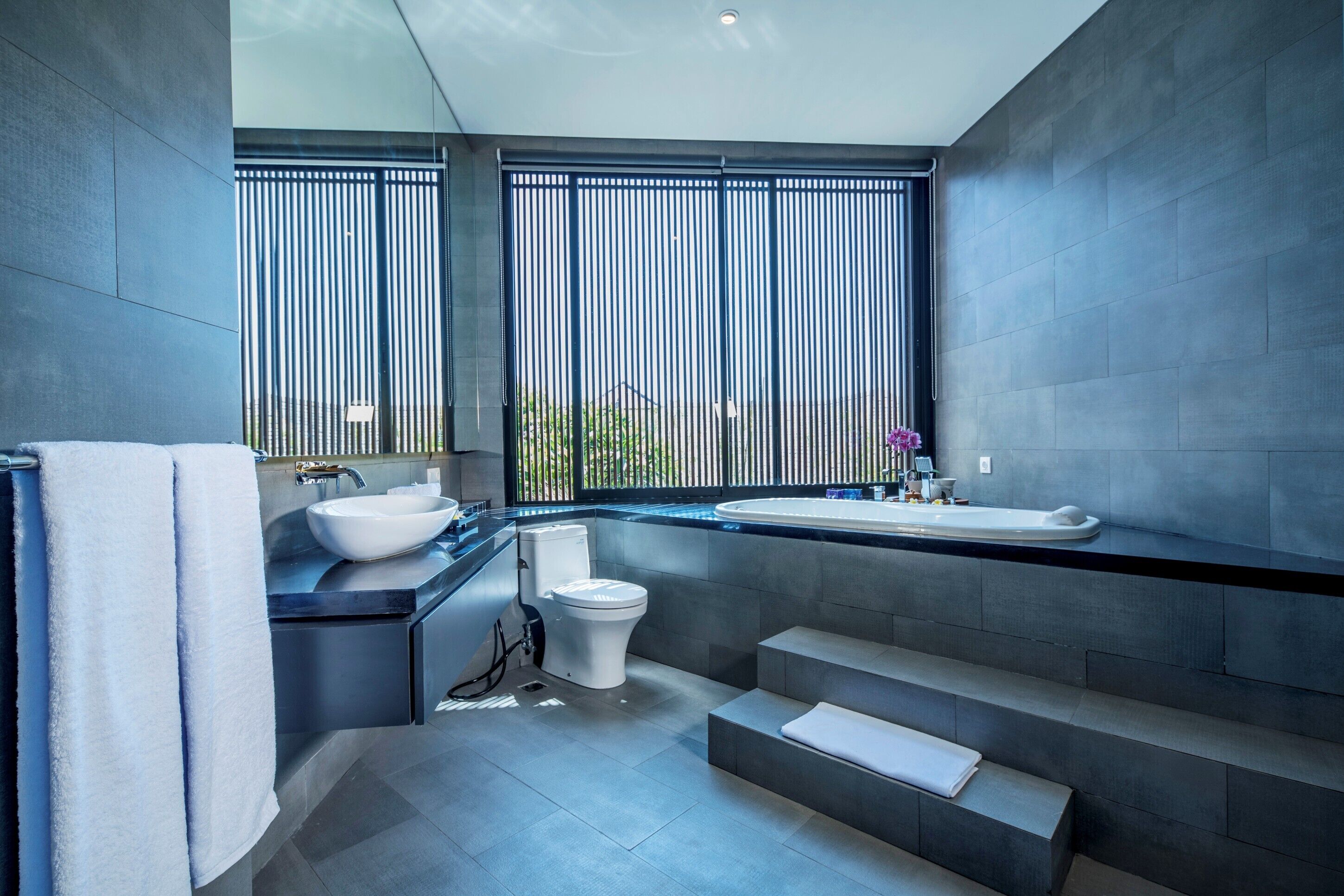 A modern bathroom with a large window, a white sink, and a toilet.