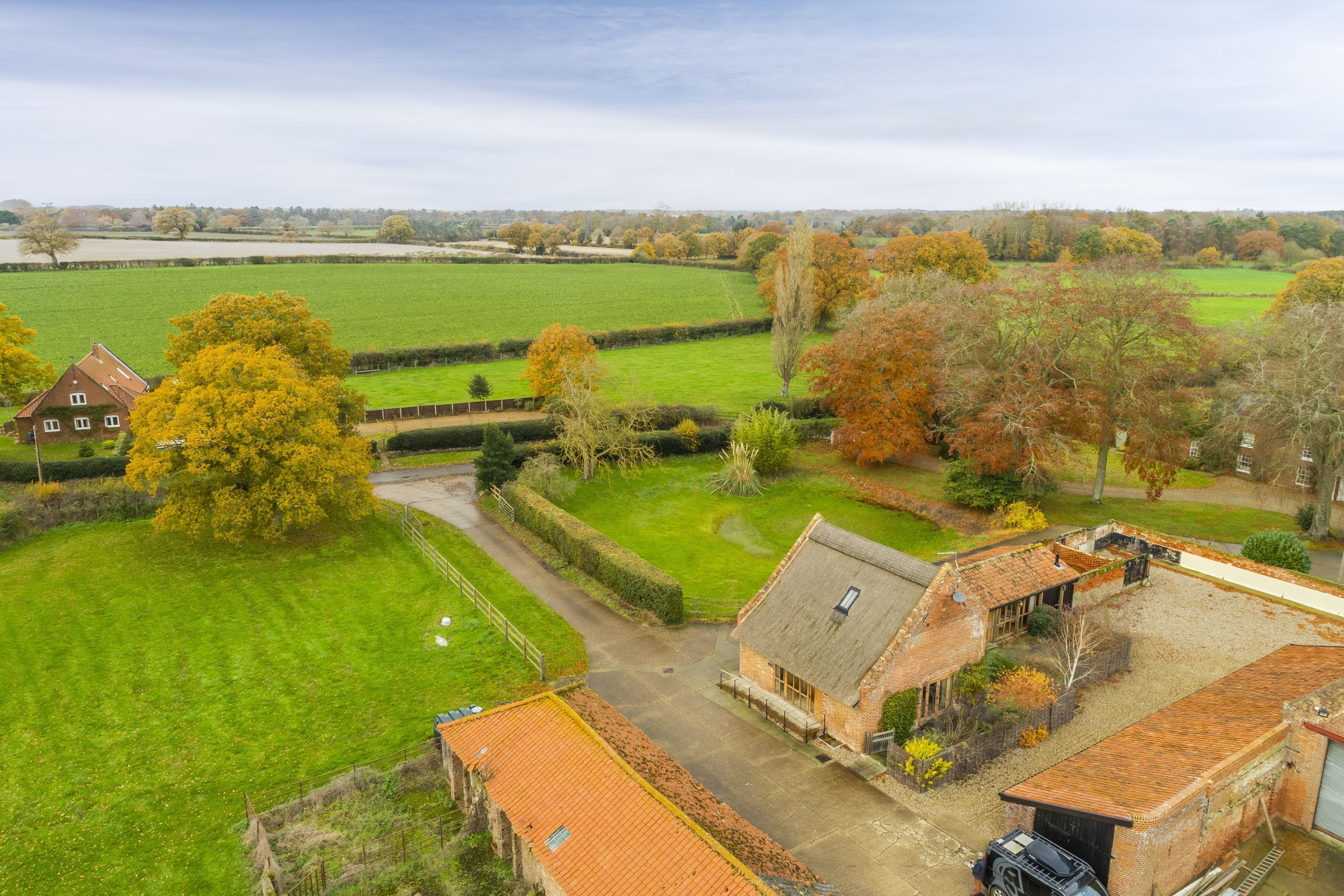 A rural property with a large green field, a brick house with a sloped roof, and a small barn.