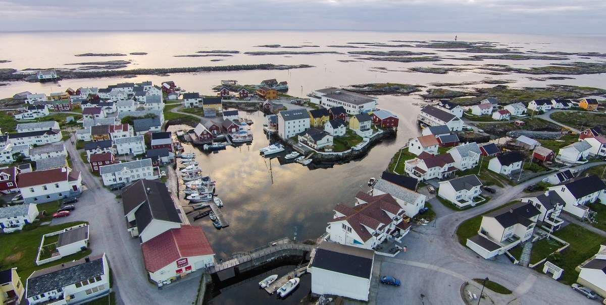 An aerial view of a coastal village with houses, a marina, and a lighthouse.
