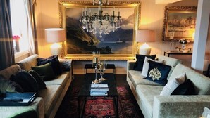A living room with two sofas, a coffee table, a chandelier, and a large framed painting of a coastal scene. - Veiholmen Brygge (Smøla)