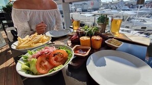 A dining table with various dishes, including fries, salad, and bread, on a boat deck with a marina view in the background. - Veiholmen Brygge (Smøla)