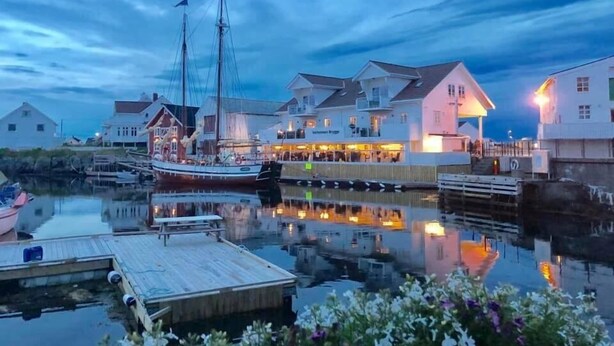 A waterfront property with a dock, a large boat, and several buildings with illuminated windows. - Veiholmen Brygge (Smøla)