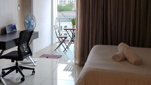 A hotel room with a bed, a desk, a chair, a fan, and a view of the outside. - Classic Studio in Kuala Lumpur 10 minutes to city center (Kuala Lumpur)