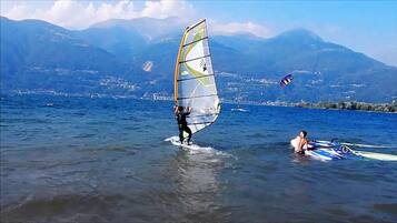 A person windsurfing on a lake with mountains in the background.