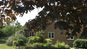 A brick house with two windows, surrounded by a well-maintained garden with various plants and a lawn. - Self Contained Stay, set within 7 acres of gated grounds, for 2 or 3 guests (Kingsfold)
