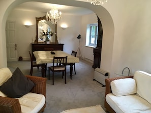 Uma área de refeições com uma mesa, cadeiras e um lustre. Há uma janela com vista para o exterior.