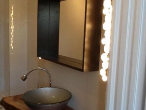 A bathroom with a vessel sink, a mirror, and a wall-mounted light fixture. - Art-Hüs (Sylt)