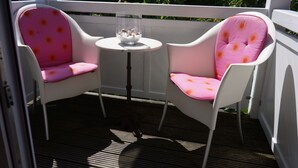 Two white chairs with pink cushions and a small table with a glass container on a wooden deck. - Art-Hüs (Sylt)
