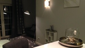 A room with a star-patterned rug, a glass fishbowl with a plant, a lamp, and a shelf with a small item. - Art-Hüs (Sylt)