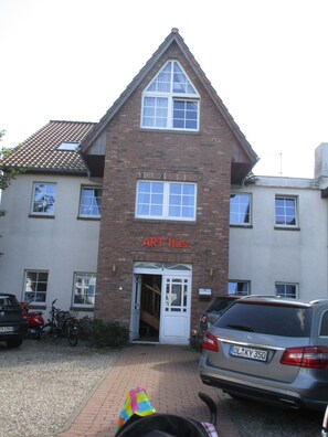 A two-story building with a brick facade and a sign reading "ART-hus". There are parked cars and a motorcycle outside. - Art-Hüs (Sylt)