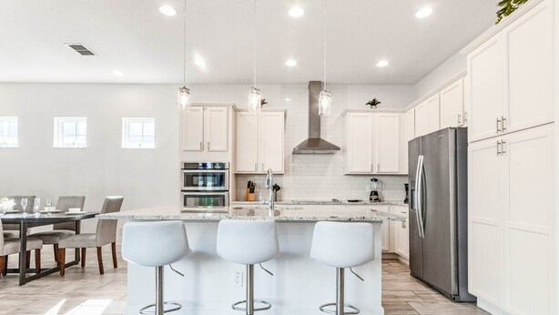 A modern kitchen with white cabinets, a stainless steel refrigerator, and a bar area with stools. - EV_1472 - 5 Bed 5.5 Bath Villa with Screened-In Private Pool, Kids Room (Kissimmee)
