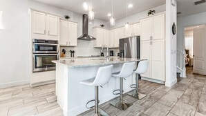 A modern kitchen with white cabinets, stainless steel appliances, a central island with bar stools, and pendant lighting. - EV_1472 - 5 Bed 5.5 Bath Villa with Screened-In Private Pool, Kids Room (Kissimmee)