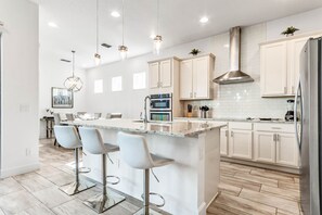 A modern kitchen with a central island, bar stools, stainless steel appliances, and light-colored cabinetry.