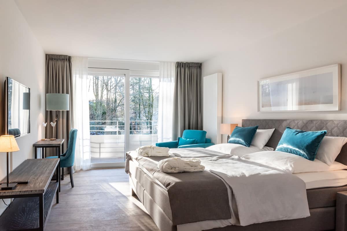 Ein Hotelzimmer mit Bett, Schreibtisch, Stuhl, einem Fenster mit Vorhängen und Blick auf Bäume.