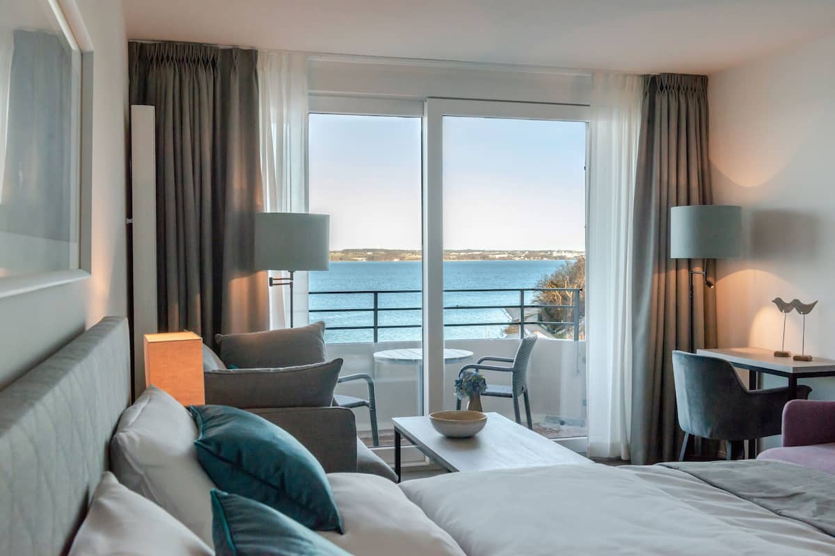 Ein Hotelzimmer mit Bett, Sofa, Esstisch, Stuhl und Meerblick.