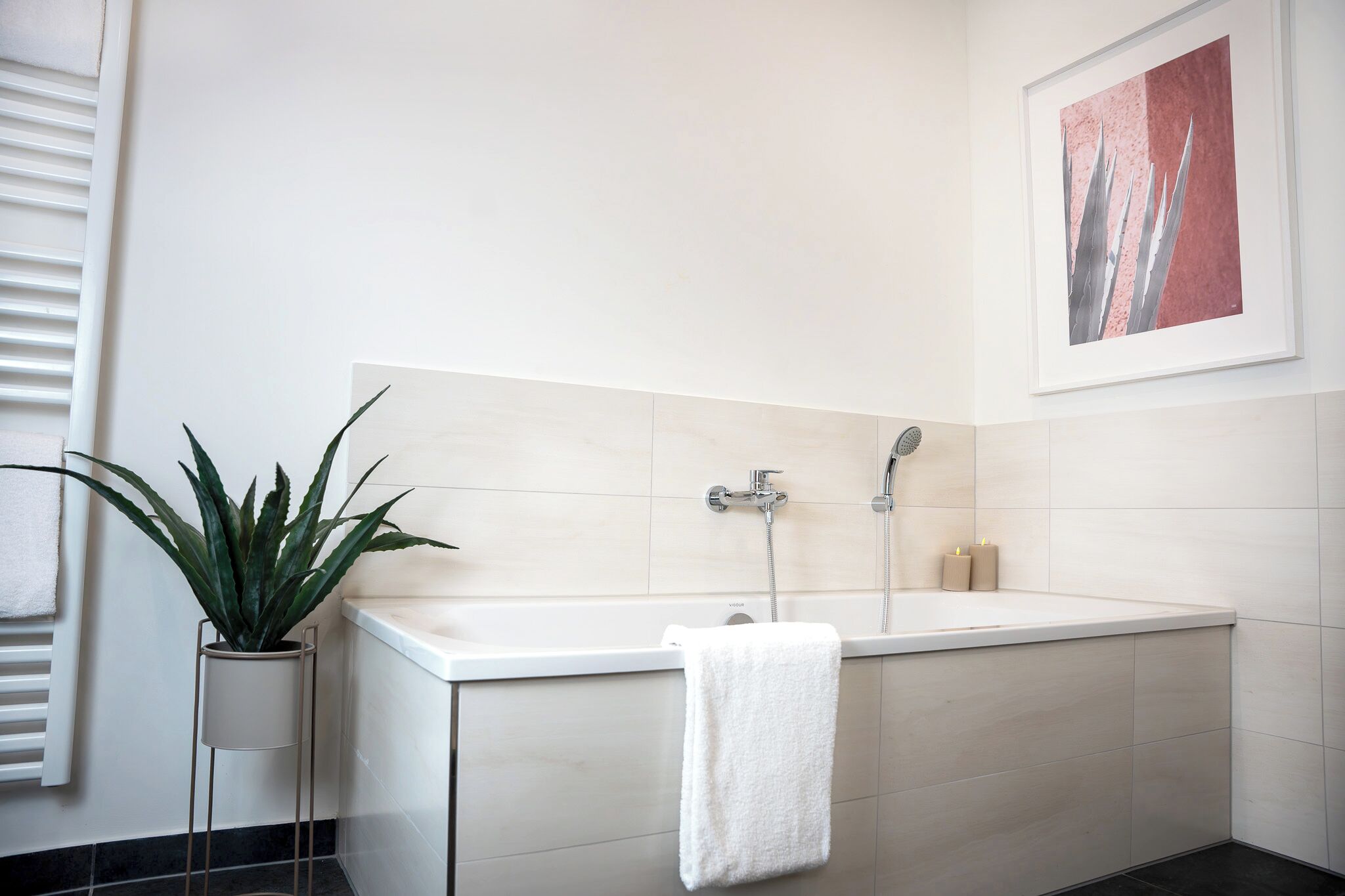 Une salle de bain moderne avec une baignoire, une plante en pot et une œuvre d’art encadrée au mur.