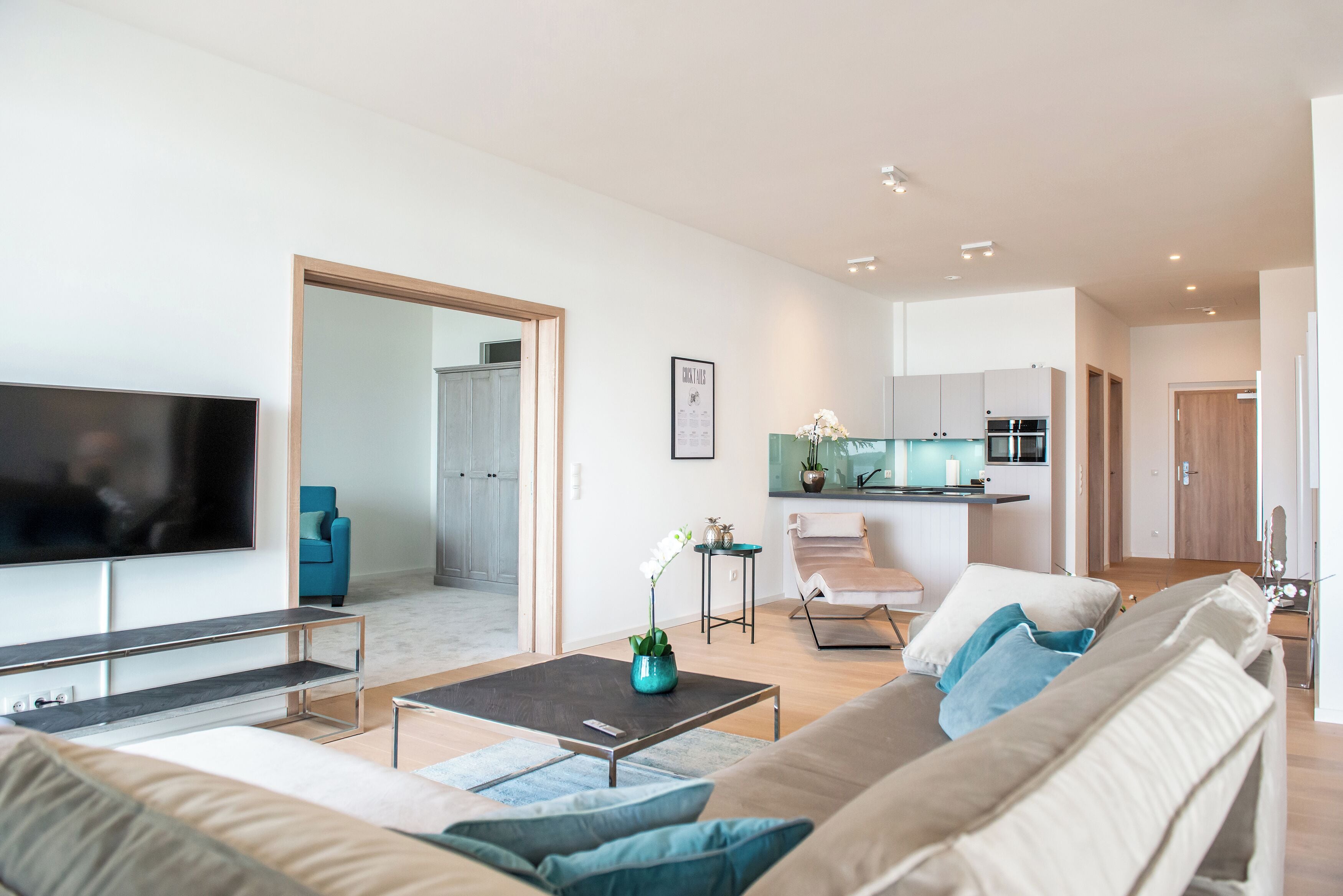 Un salon moderne avec un téléviseur à écran plat, un canapé, une table basse et une cuisine en arrière-plan.