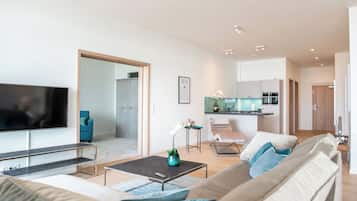 Una sala de estar moderna con un televisor de pantalla plana, un sofá, una mesa de centro y una cocina al fondo.