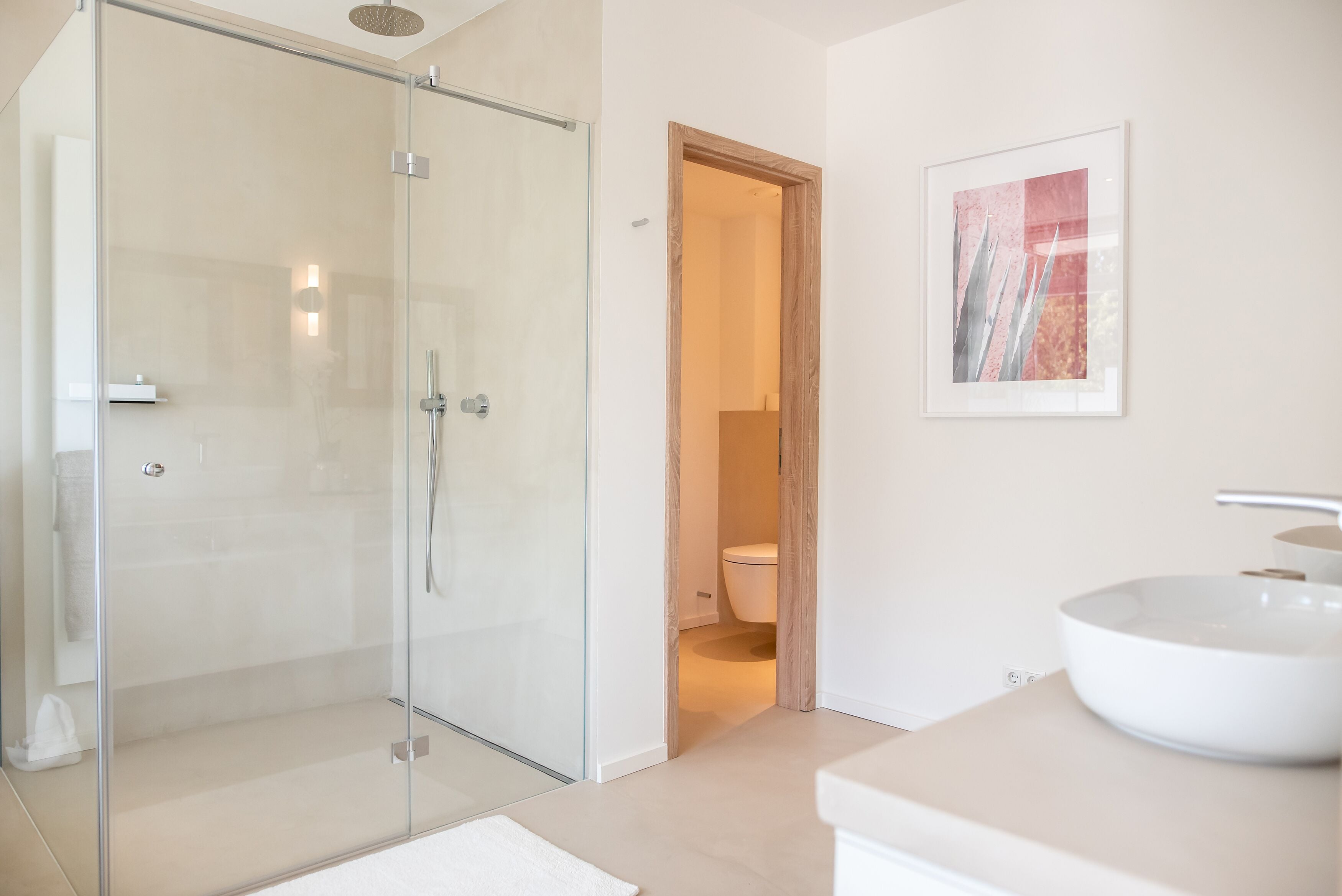 Un baño moderno con cabina de ducha de vidrio, un lavabo blanco y una obra de arte enmarcada en la pared.
