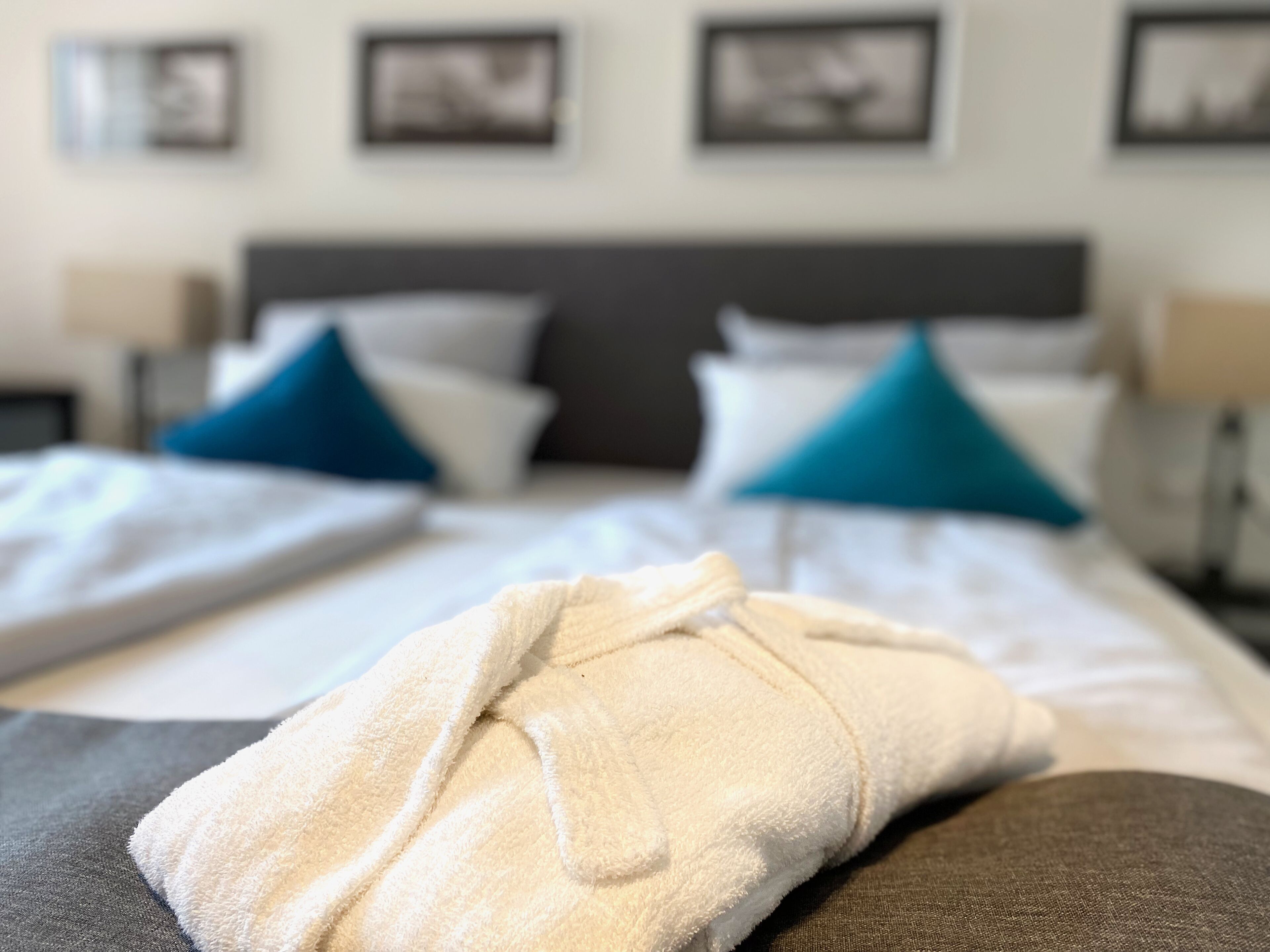 A neatly made bed with white and blue pillows, a grey headboard, and a white bathrobe on the bed.