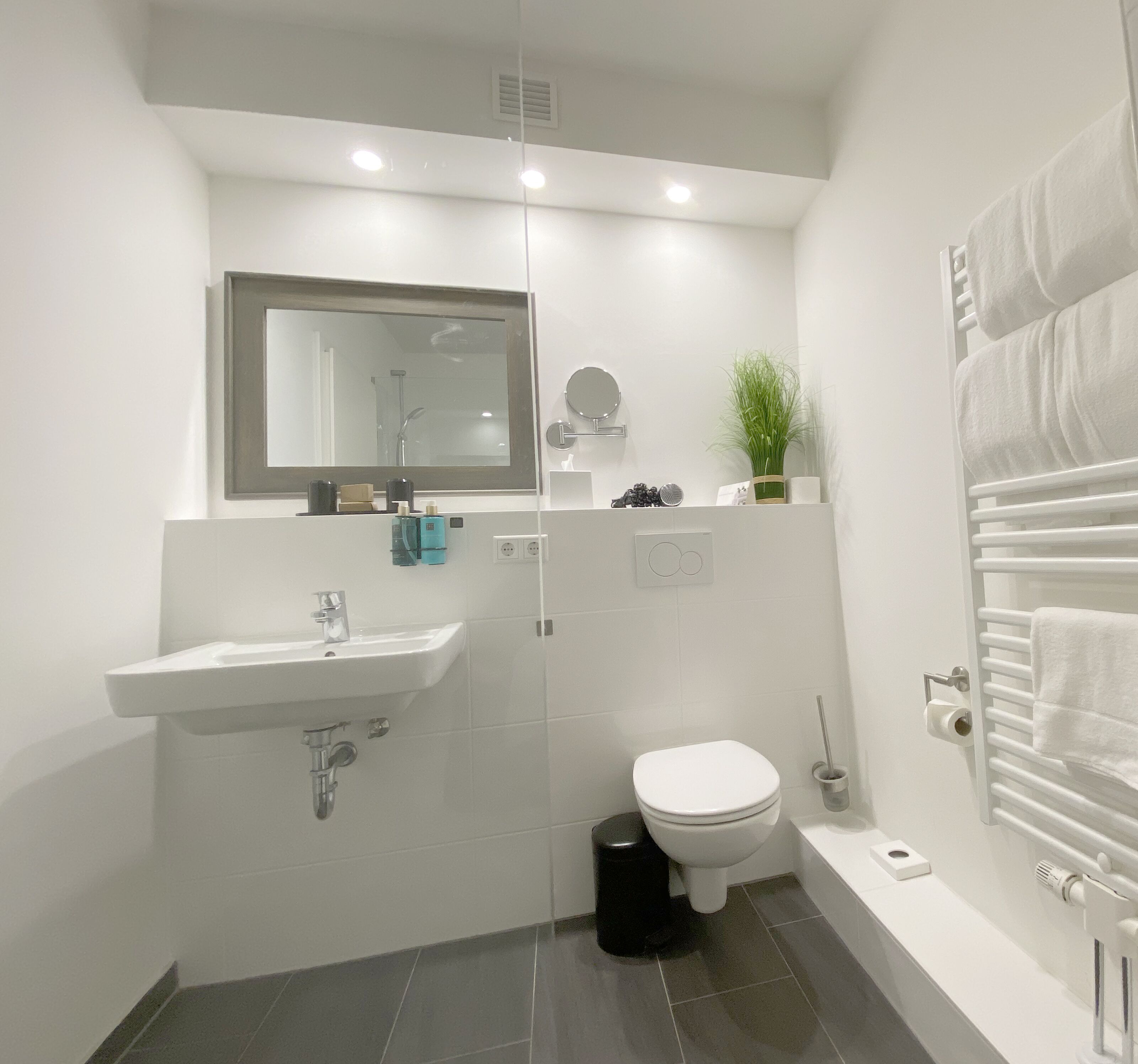 Uma casa de banho moderna com uma sanita, um lavatório branco, um espelho e um porta-toalhas.