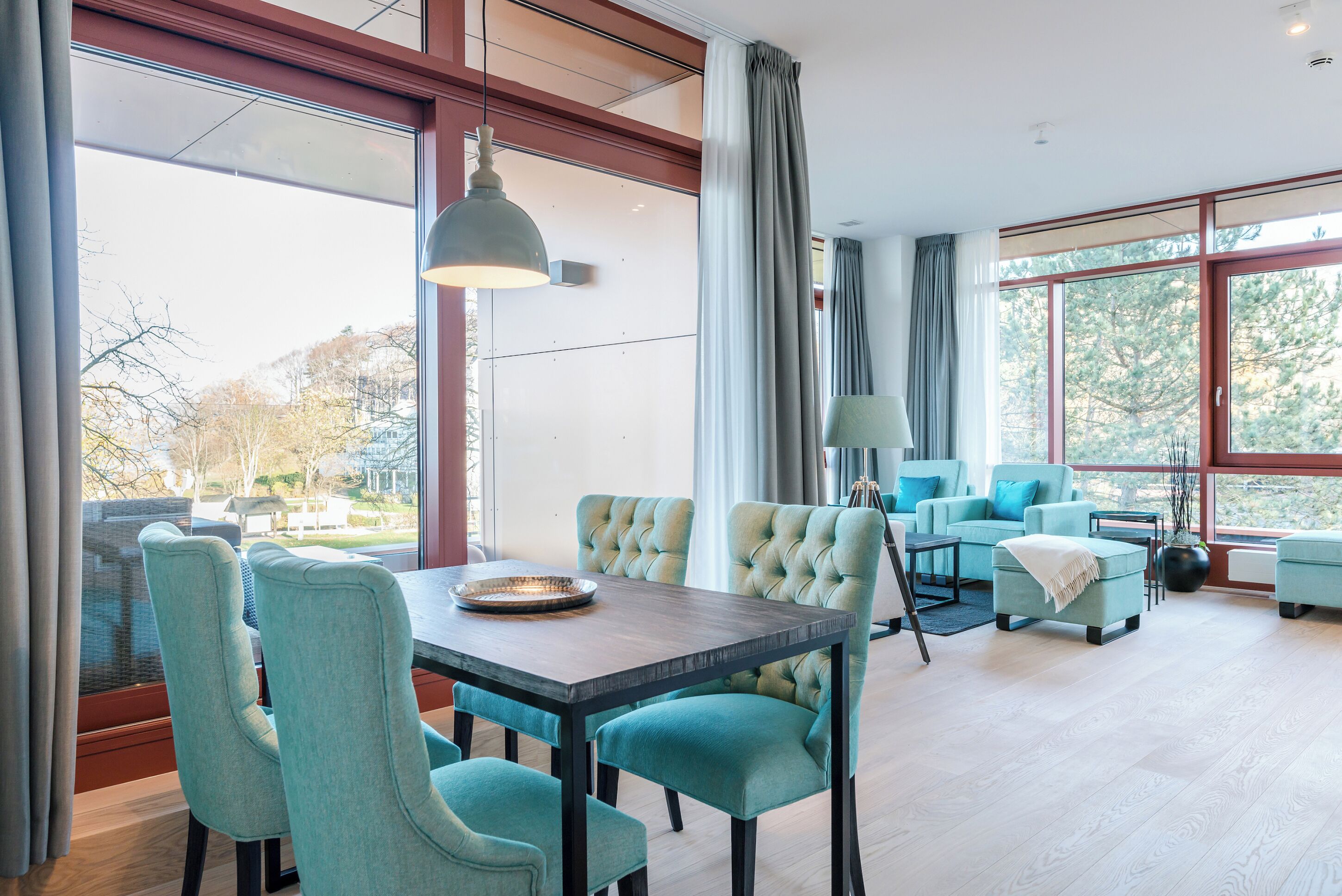 A modern dining area with a table and chairs, a sofa set, and large windows with curtains.
