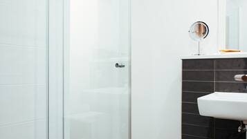 Un baño moderno con cabina de ducha de vidrio, un lavamanos blanco y una pared revestida de azulejos negros.