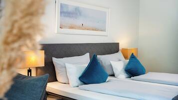 Habitación de hotel con cama, almohadas, cabecera, cuadro colgado en la pared y lámparas de noche.