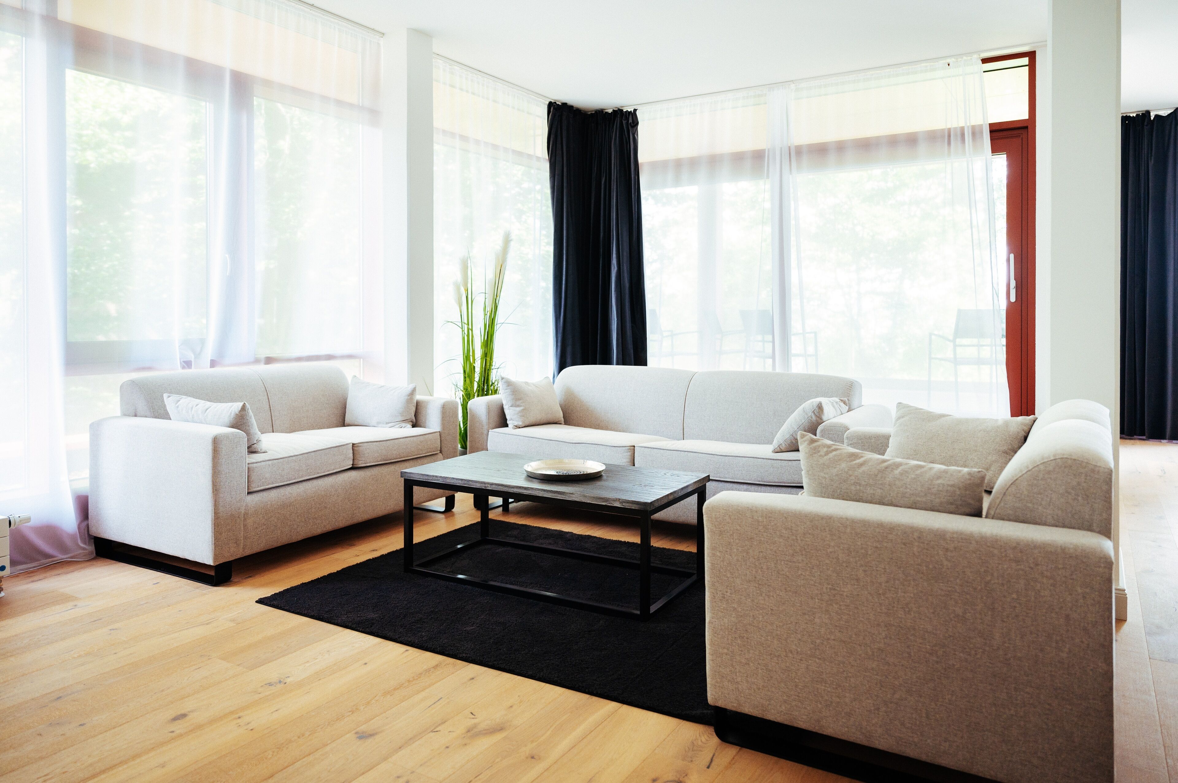A modern living room with two sofas, a coffee table, and large windows with sheer curtains.