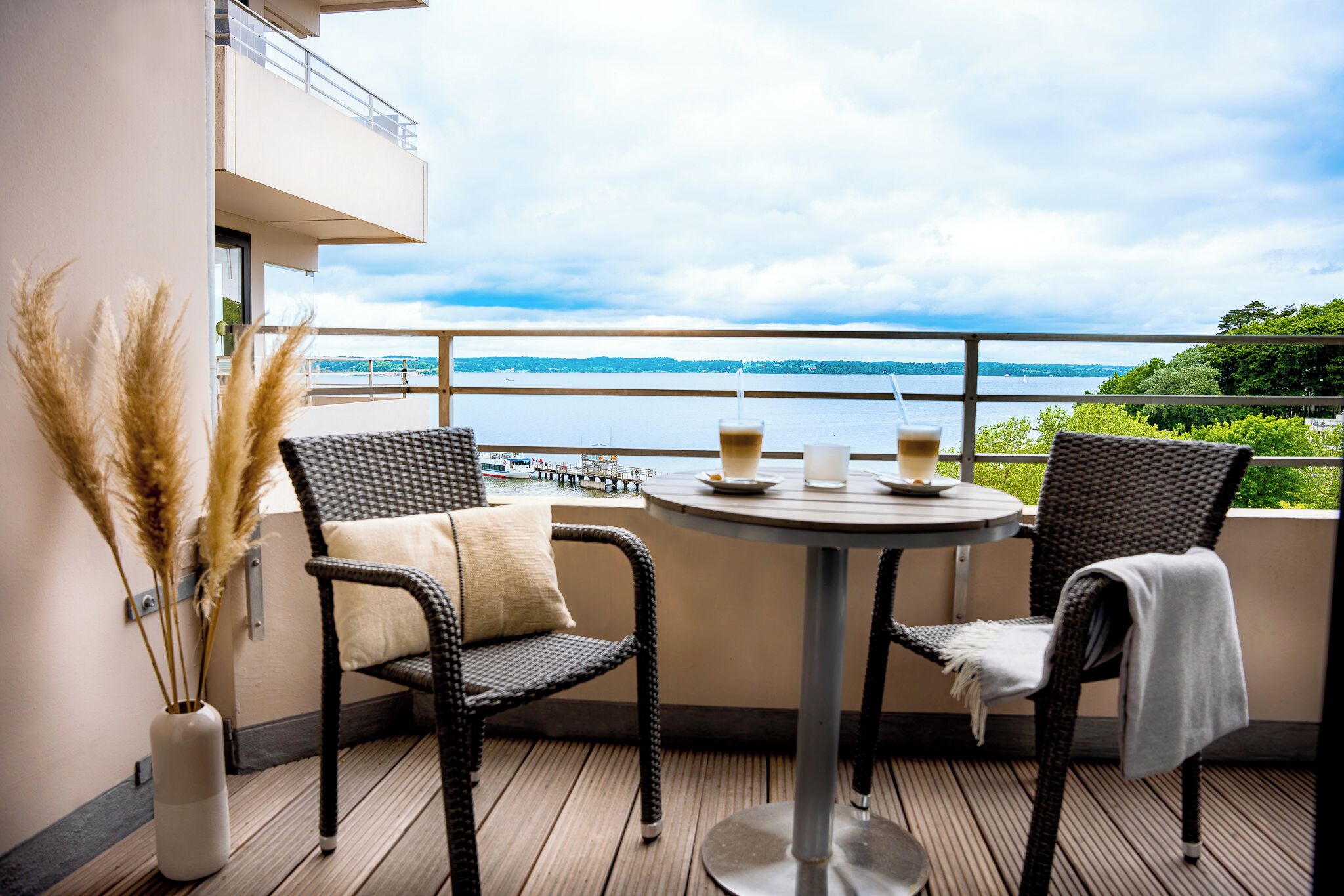 Un balcon avec des fauteuils en osier, une table ronde et une vue sur un lac.