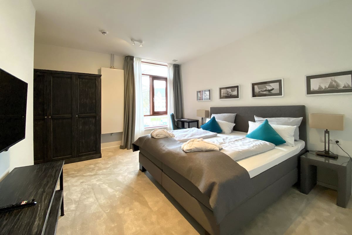 Ein modernes Hotelzimmer mit einem großen Bett, einem dunklen Holzschrank, einem Schreibtisch und einem Fernseher.