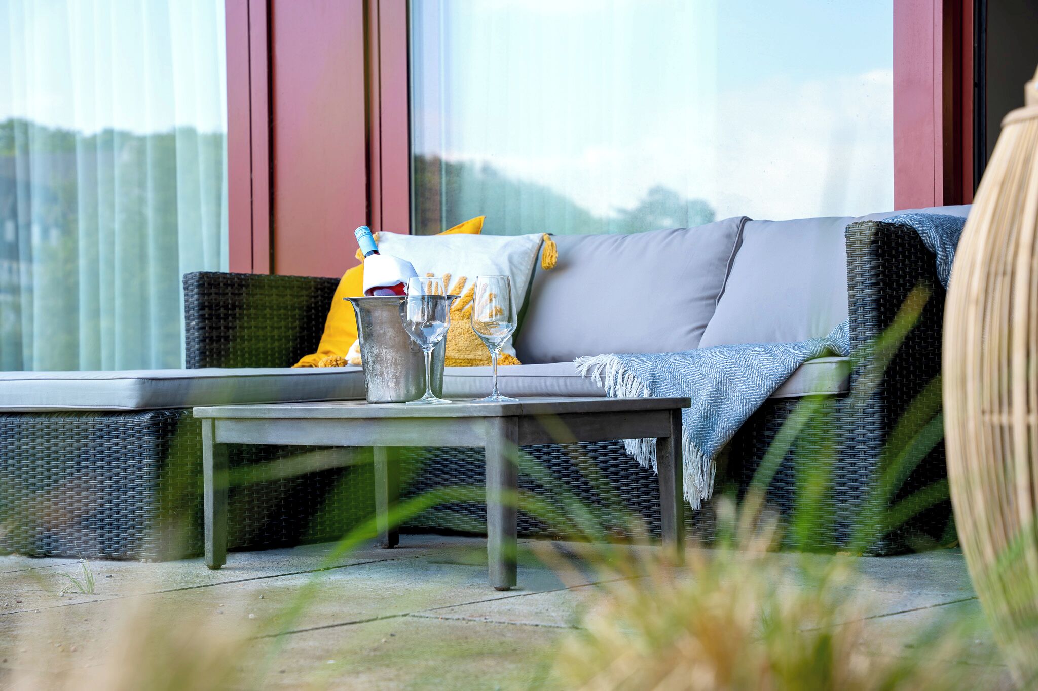 A wicker sofa with cushions, a metal table with a glass, and a wicker basket.