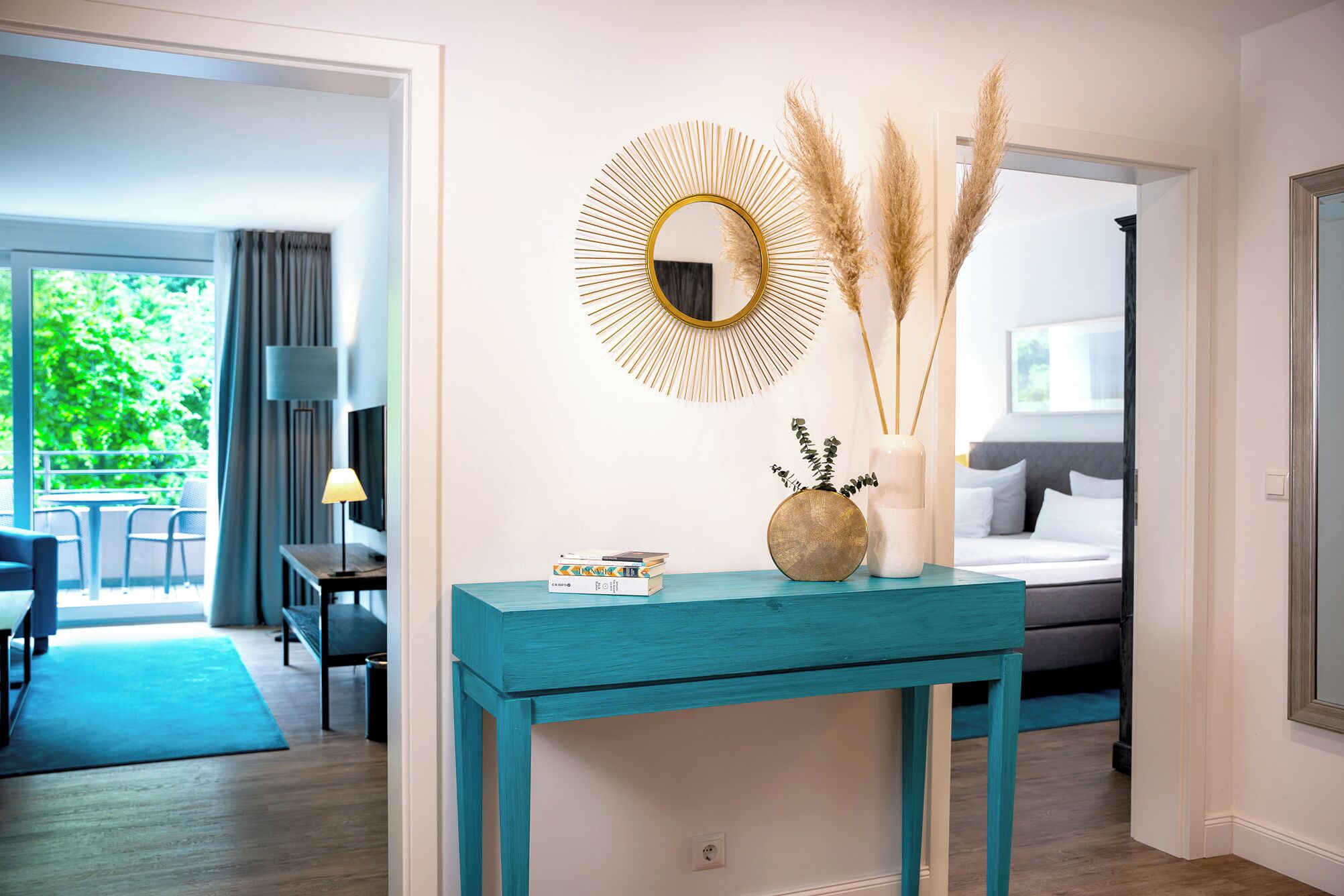 Una habitación moderna con una consola azul turquesa, un espejo dorado y plantas decorativas.