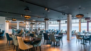 Ein geräumiges Restaurant mit hohen Decken, moderner Pendelleuchten und Meerblick.