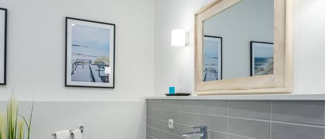A modern bathroom with a large mirror, a white sink, and a towel rack.