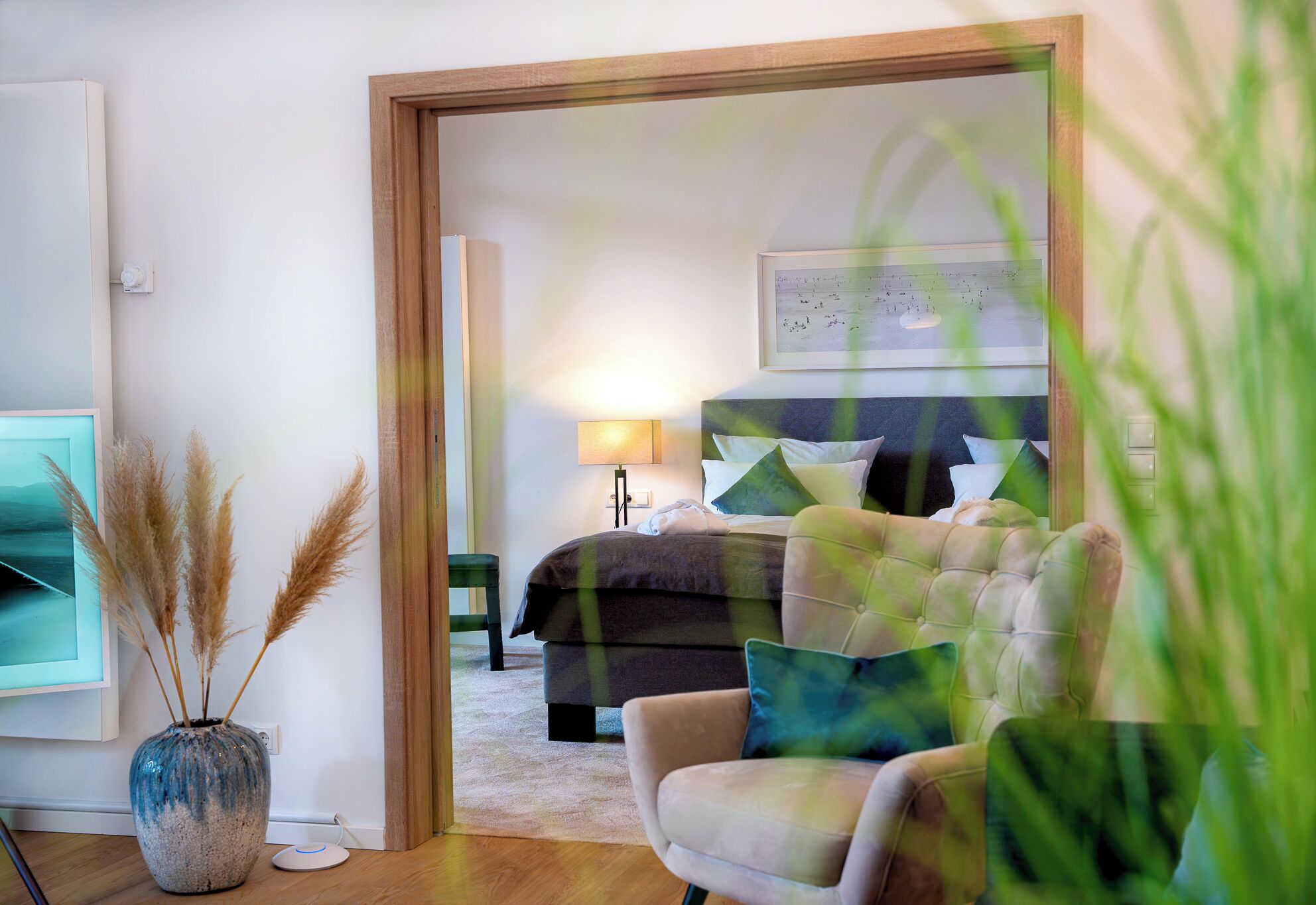A bedroom with a bed, bedside table, lamp, and a view of the outside.