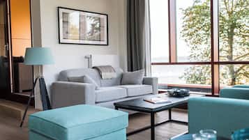 A modern living room with a sofa, ottoman, and coffee table, a framed picture on the wall, and a large window with a view.