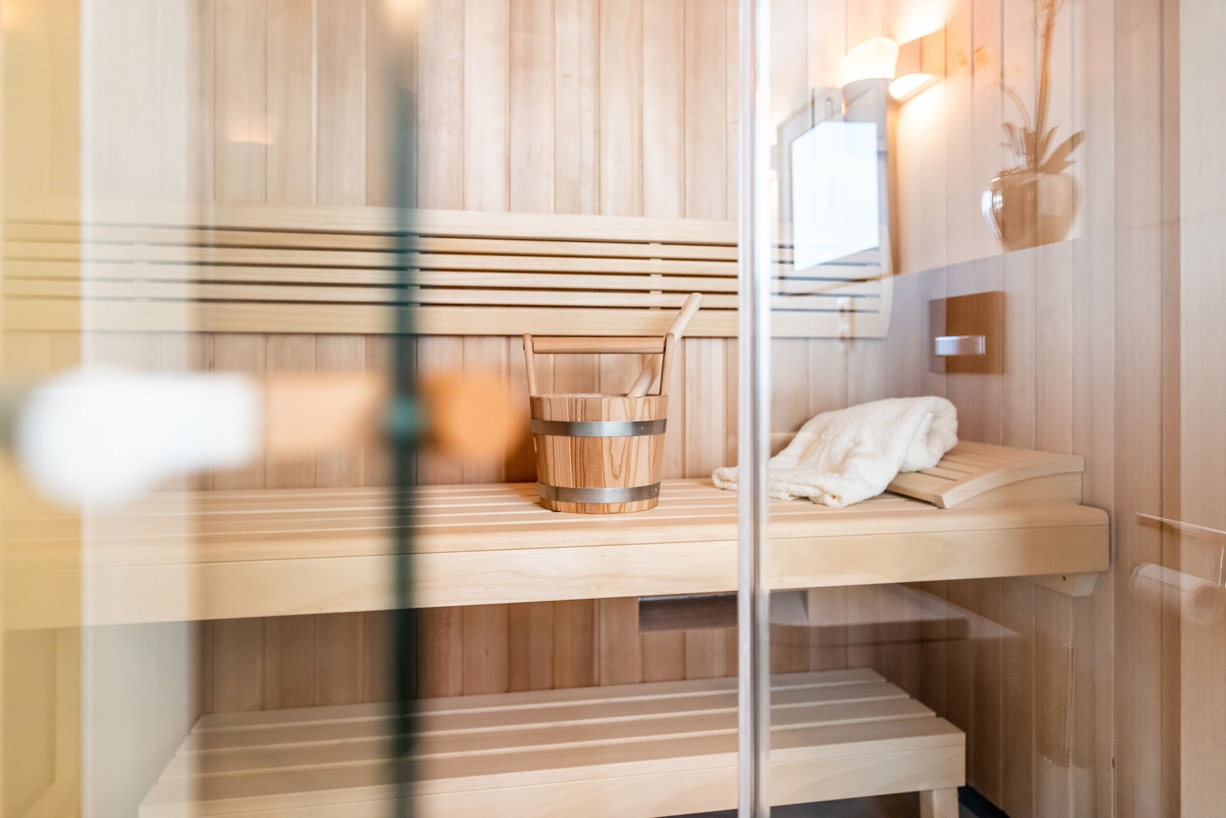 Un sauna avec des bancs en bois, un seau en bois et une serviette posée sur une étagère.