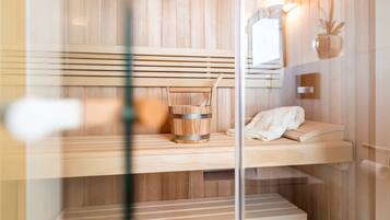 Een sauna met houten banken, een houten emmer en een handdoek op een plank.