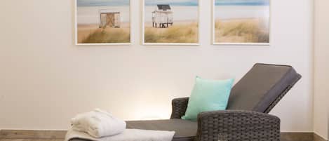 A room with a reclining chair, a small table with fruit, and three beach-themed wall art pieces.