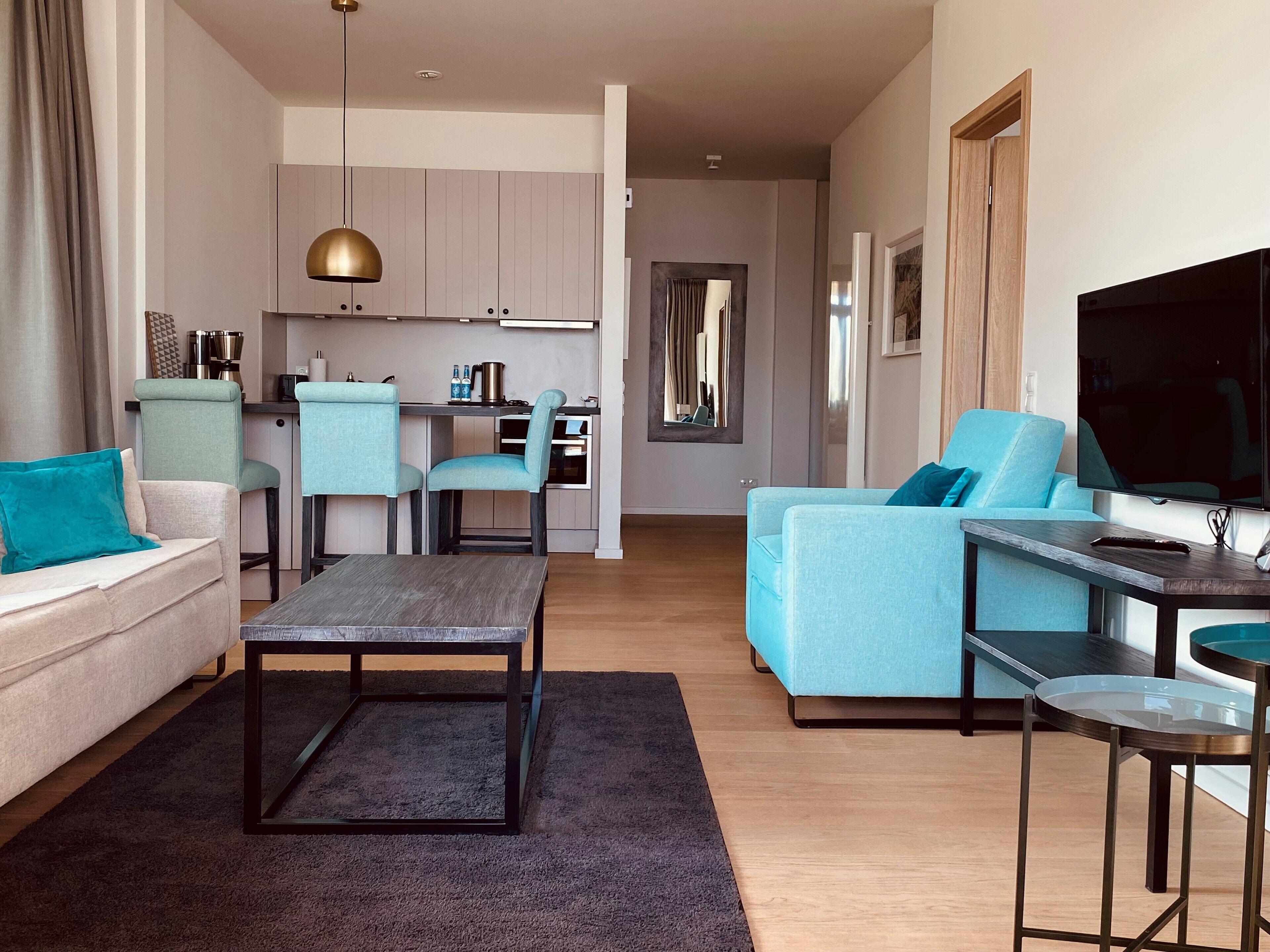 A modern living room with a sofa, a coffee table, and a TV. There is a kitchen area with a dining table and chairs.