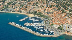 Vue aérienne d’une marina côtière où de nombreux bateaux sont amarrés, entourée de bâtiments résidentiels et d’une plage.