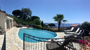 Un espace piscine doté d’une terrasse en pierre, de chaises longues et offrant une vue sur la mer.