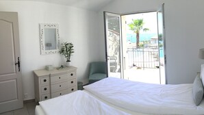Une chambre à coucher comprenant un lit, une commode, une chaise, un miroir et un balcon avec vue sur la mer.