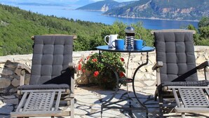 Deux fauteuils confortables sont placés face à une table sur laquelle se trouvent une cafetière et des tasses, et l’ensemble offre une vue magnifique sur un lac et des montagnes.