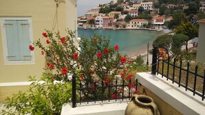 Un balcon donnant sur une ville côtière, un arbuste fleuri et un grand vase.