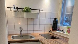 Cocina compacta con un lavamanos de acero inoxidable, encimera de madera, armarios blancos y ventana con vistas a la nieve.