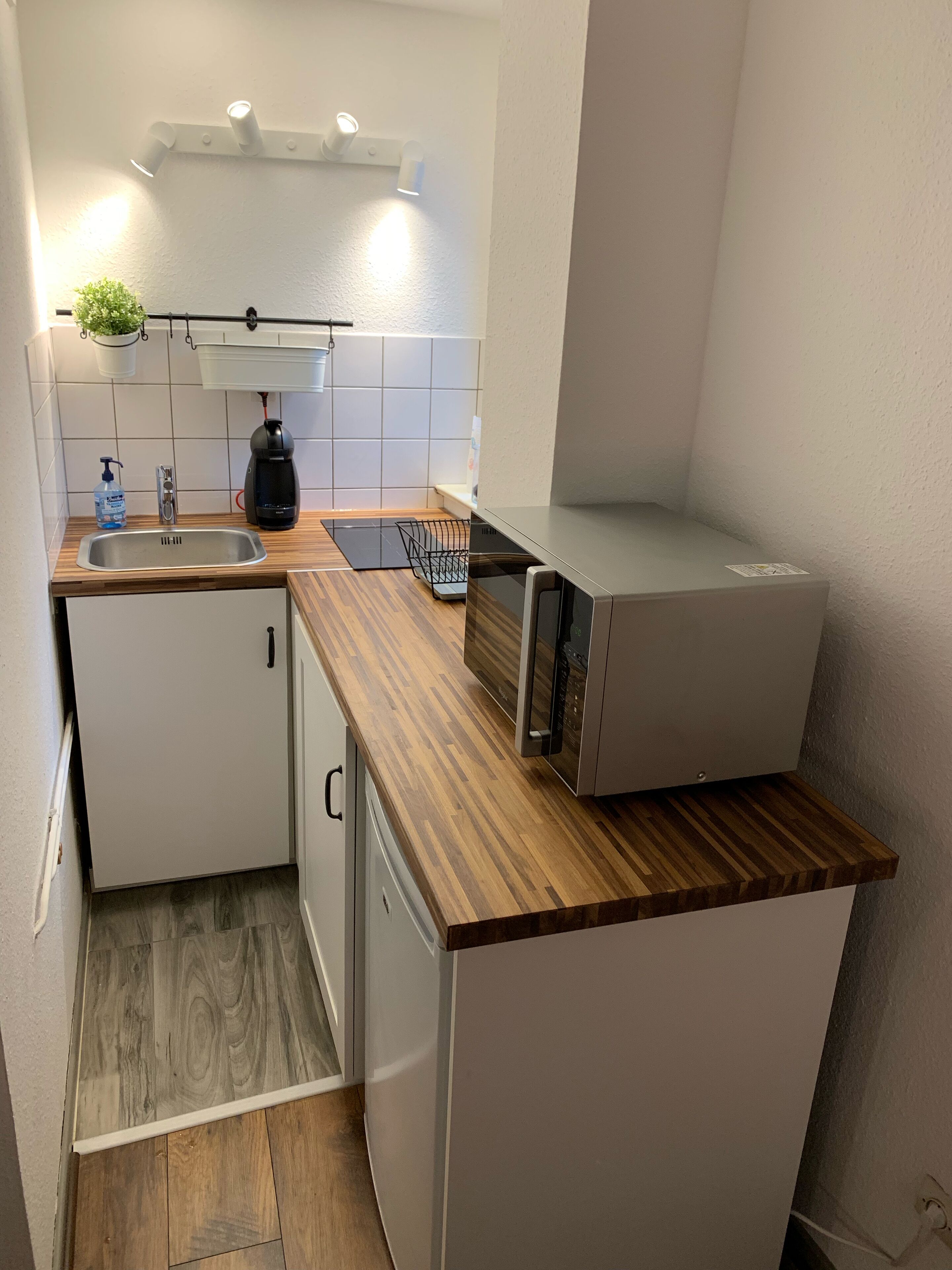 A compact kitchen with a wooden countertop, a built-in dishwasher, and a microwave.